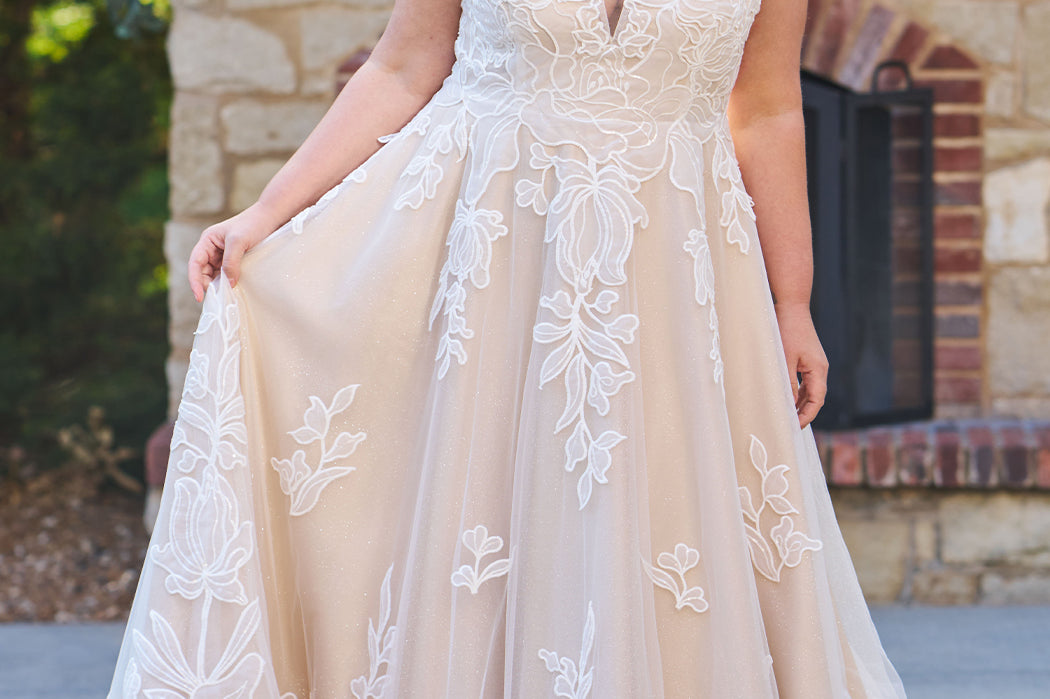 Plus size A-line oversized floral weding dress in ivory or champagne. Style MB2525 from Michelle Bridal by Sydney's Closet has illusions straps covered in appliques, natural waisltine, long flowy A-line skirt and long train with covered buttons.