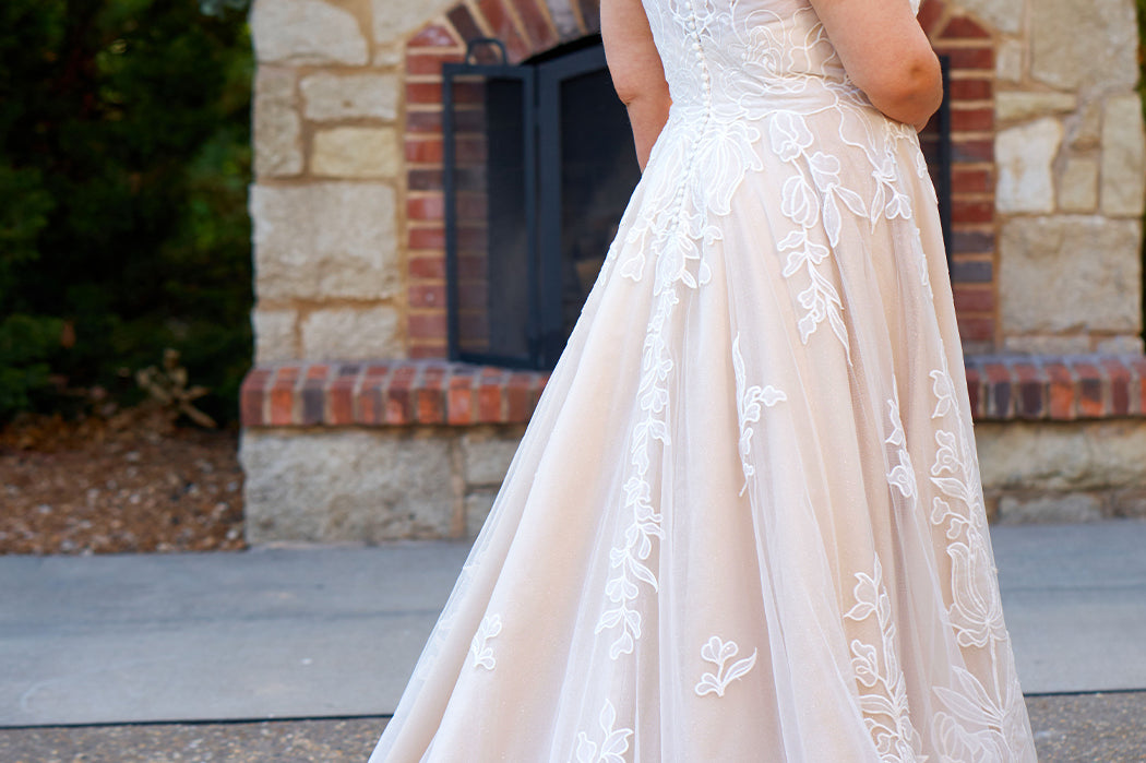 Plus size A-line oversized floral weding dress in ivory or champagne. Style MB2525 from Michelle Bridal by Sydney's Closet has illusions straps covered in appliques, natural waisltine, long flowy A-line skirt and long train with covered buttons.