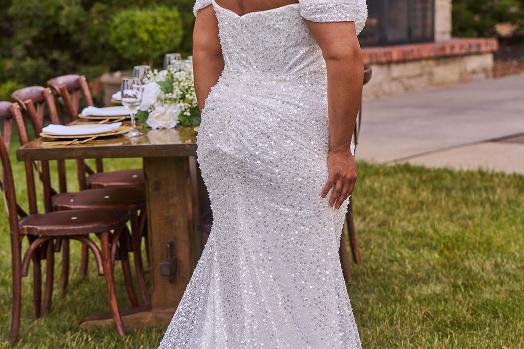 Sexy curvy plus-size fitted formal bridal dress with drape sleeves, exposed boning and ruching.  Beaded bling fabric with sequins, stones and pearls.  Long train and ruching on the buttocks. MB2528 from Michelle Bridal by Sydney's Closet.