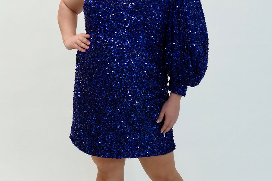 This is SC8133 in our Sydney's Closet Homecoming collection. This plus size party dress comes in black, blue, purple, and red! This dress has a one shoulder long sleeve pouf sleeve, a cutout bodice, and a natural waistline. This fitted all over sequin dress has the spotlight as the most perfect dress for this homecoming season!