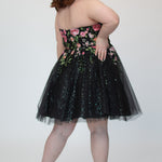 SC8137 Back view. Black sparkle tulle short a-line party dress with pink floral embroidered roses. Strapless sweetheart neckline, long invisible center back zipper.  Available only in black floral. Curvy sizes 10-32. Model in picture is 5 foot 9 inches and a size 16.