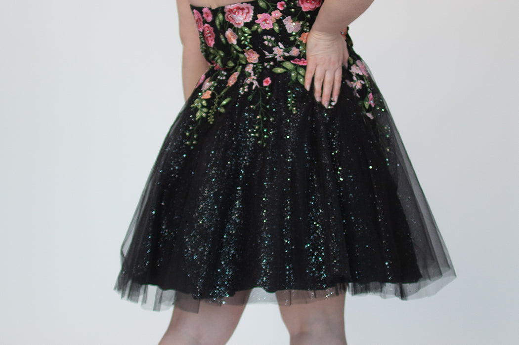 SC8137 Back view. Black sparkle tulle short a-line party dress with pink floral embroidered roses. Strapless sweetheart neckline, long invisible center back zipper.  Available only in black floral. Curvy sizes 10-32. Model in picture is 5 foot 9 inches and a size 16.