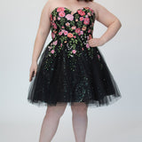 SC8137 Front view. Black sparkle tulle short a-line party dress with pink floral embroidered roses. Strapless sweetheart neckline, long invisible center back zipper.  Available only in black floral. Curvy sizes 10-32. Model in picture is 5 foot 9 inches and a size 16.