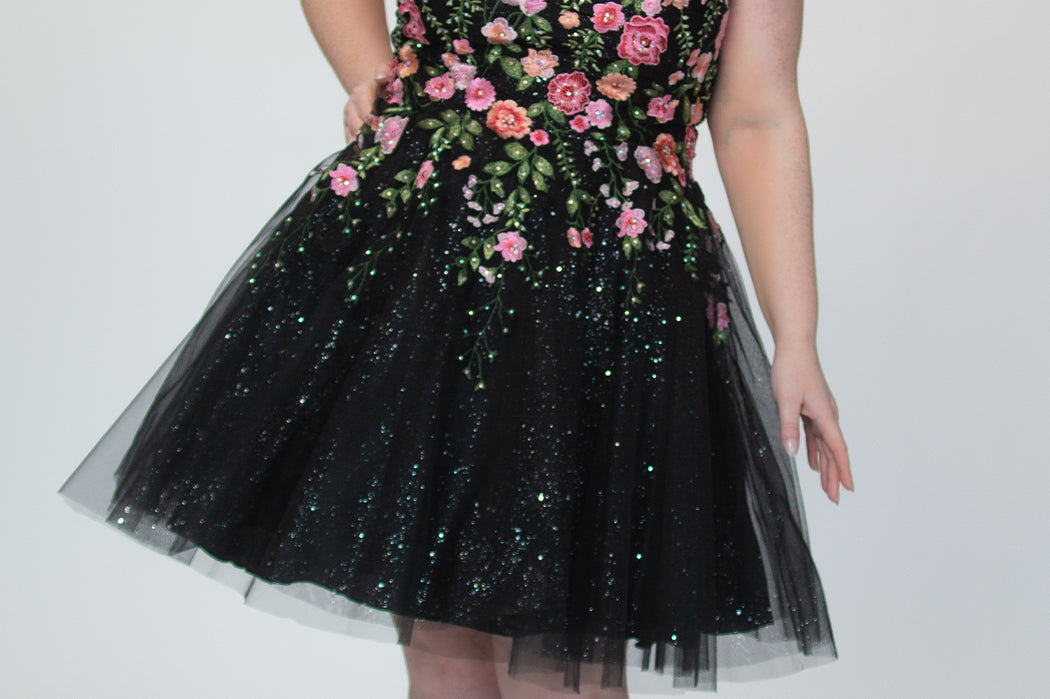 SC8137 Front view. Black sparkle tulle short a-line party dress with pink floral embroidered roses. Strapless sweetheart neckline, long invisible center back zipper.  Available only in black floral. Curvy sizes 10-32. Model in picture is 5 foot 9 inches and a size 16.