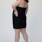 Short fitted black party dress SC8143 by Sydney's Closet. Back view.  Strapless, exposed boning basque waist and ruched fitted skirt in shimmer stretch knit. Availability in black, purple, red, ivory, green and royal. Model in picture is 5'9.