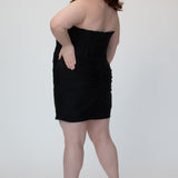 Short fitted black party dress SC8143 by Sydney's Closet. Back view.  Strapless, exposed boning basque waist and ruched fitted skirt in shimmer stretch knit. Availability in black, purple, red, ivory, green and royal. Model in picture is 5'9.