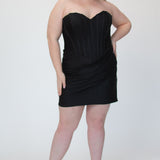 Short fitted black party dress SC8143 by Sydney's Closet. Front view.  Strapless, exposed boning basque waist and ruched fitted skirt in shimmer stretch knit. Availability in black, purple, red, ivory, green and royal. Model in picture is 5'9.