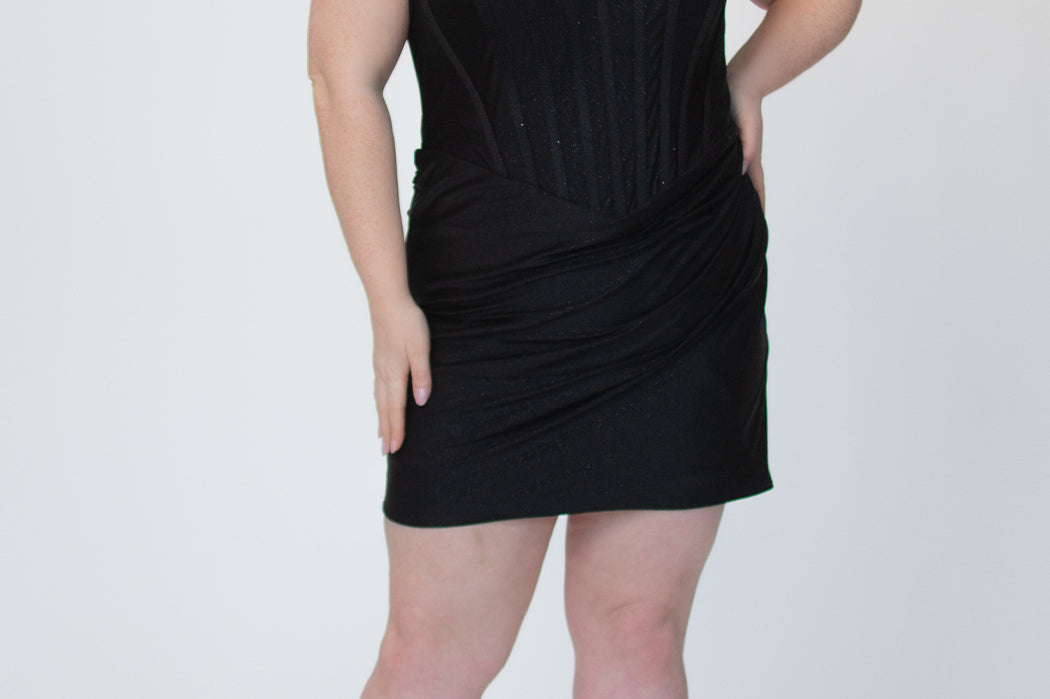 Short fitted black party dress SC8143 by Sydney's Closet. Front view.  Strapless, exposed boning basque waist and ruched fitted skirt in shimmer stretch knit. Availability in black, purple, red, ivory, green and royal. Model in picture is 5'9.