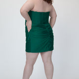 Short fitted green party dress SC8143 by Sydney's Closet. Back view.  Strapless, exposed boning basque waist and ruched fitted skirt in shimmer stretch knit. Availability in black, purple, red, ivory, green and royal. Model in picture is 5'9.