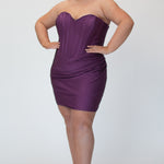 Short fitted purple party dress SC8143 by Sydney's Closet. Front view.  Strapless, exposed boning basque waist and ruched fitted skirt in shimmer stretch knit. Long invisible center back zipper. Availability in black, purple, red, ivory, green and royal. Model in picture is 5'9.