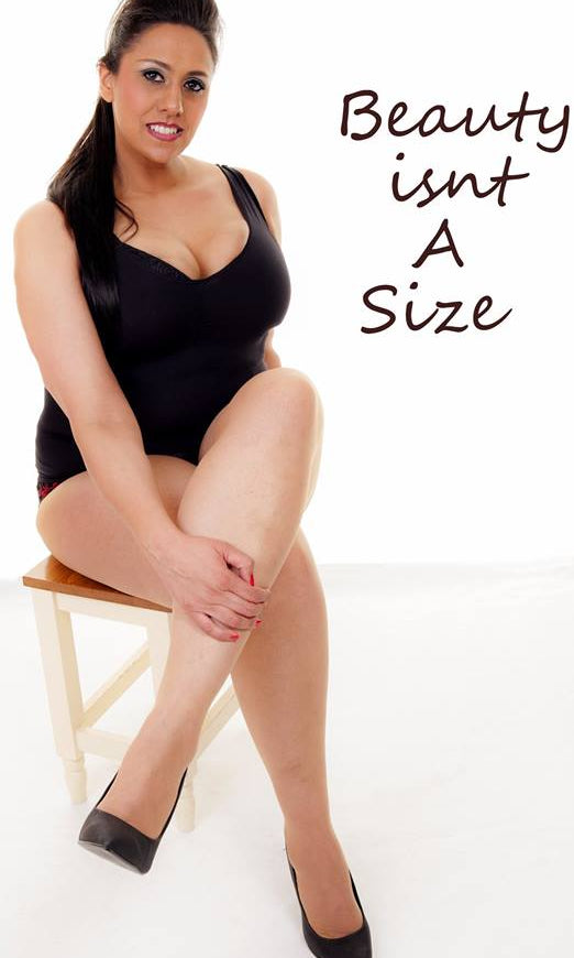 Plus Size model Sharon D from the UK wearing a black body suit, heels and sitting on a chair. Text says "Beauty isn't a size"