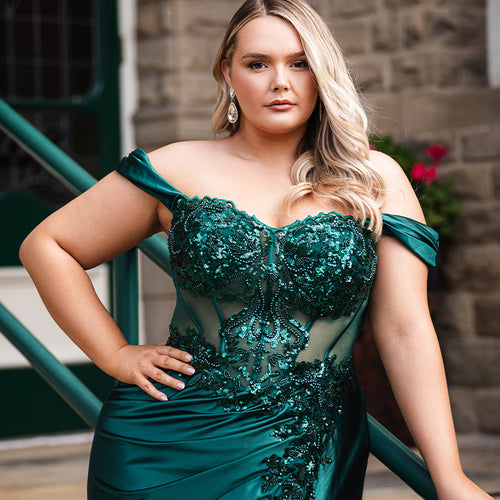 Sydney's Closet UK Capsule collection UK2616 emerald green plus size prom dress

Woman in a teal evening gown standing on steps with a stone wall and green railing in the background.
