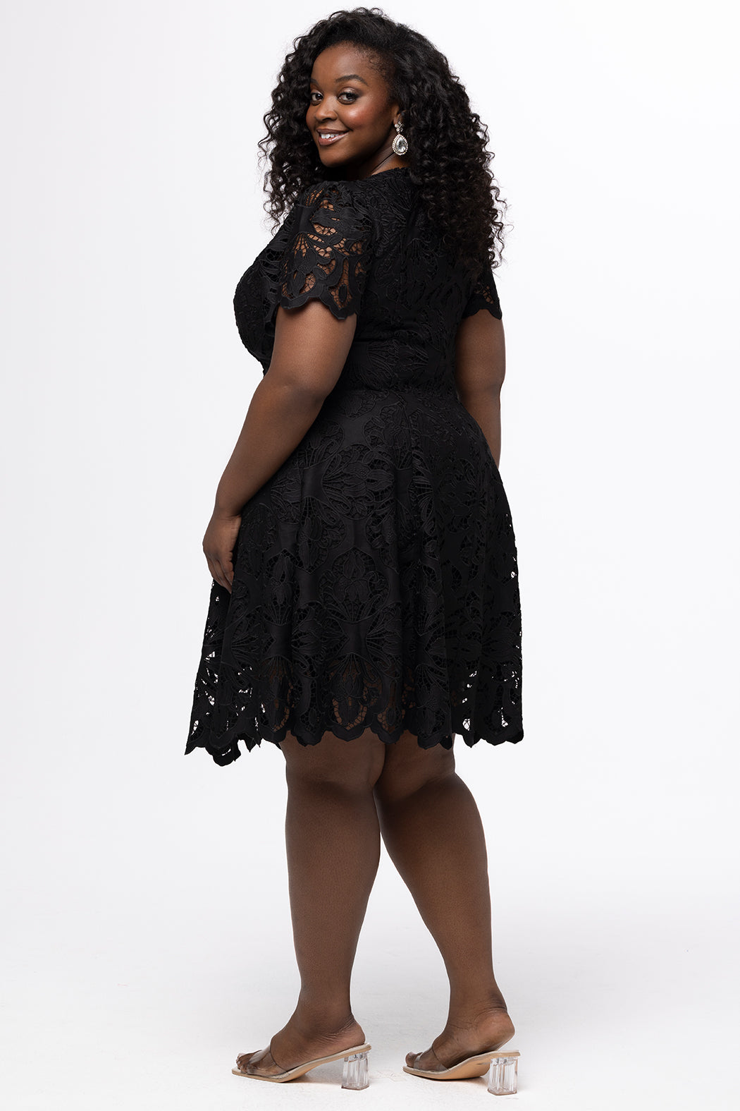 Plus size little black dress made of Guipure lace. Short sleeves, scoop neckline and center back zipper. CE2601 available in sizes 14-24 in black. Celebrations by Sydney's Closet.