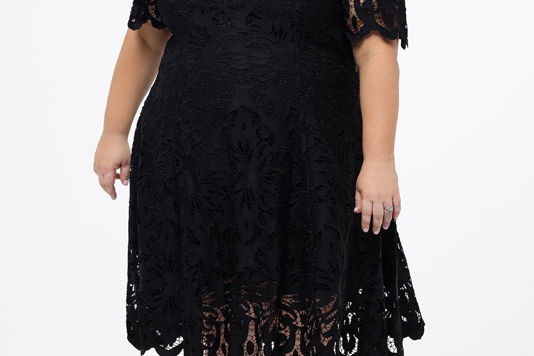 Plus size little black dress made of Guipure lace. Cap sleeves, scoop neckline and center back zipper. CE2601 available in sizes 14-24 in black. Celebrations by Sydney's Closet.