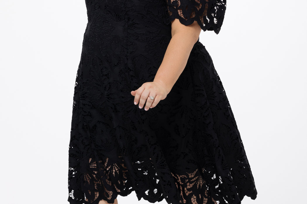Plus size little black dress made of Guipure lace. Cap sleeves, scoop neckline and center back zipper. CE2601 available in sizes 14-24 in black. Celebrations by Sydney's Closet.