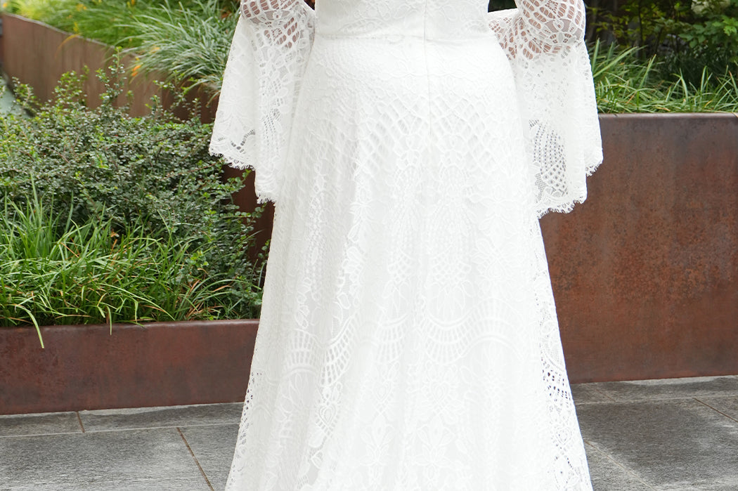 Boho crochet lace plus size wedding dress with V-neckline, illusion lace straps, illusion long flowy bell sleeves, natural wiasltine and slim A-line skirt finished with scalloped eyelash hem.  Available in ivory. Celebrations by Sydney's Closet style CE2604