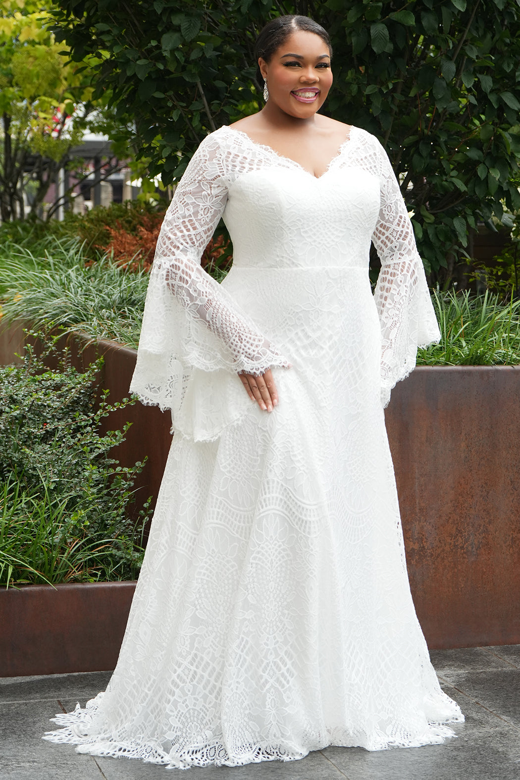 Boho crochet lace plus size wedding dress with V-neckline, illusion lace straps, illusion long flowy bell sleeves, natural wiasltine and slim A-line skirt finished with scalloped eyelash hem.  Available in ivory. Celebrations by Sydney's Closet style CE2604