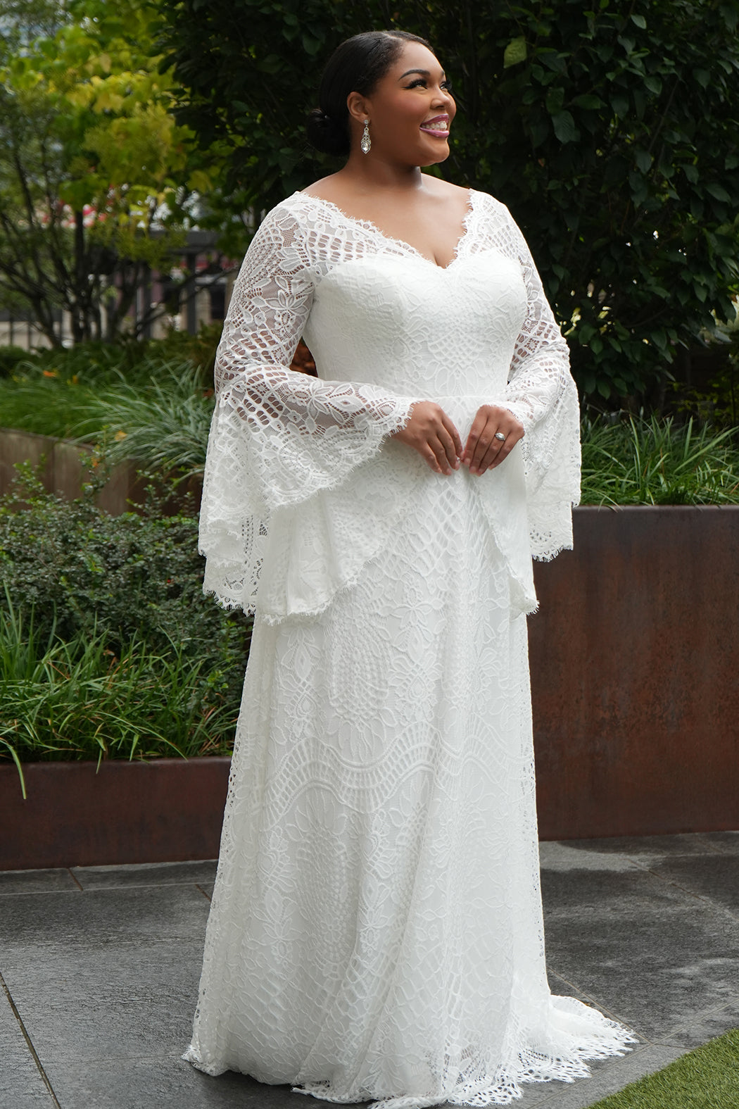 Boho crochet lace plus size wedding dress with V-neckline, illusion lace straps, illusion long flowy bell sleeves, natural waistline and slim A-line skirt finished with scalloped eyelash hem.  Available in ivory. Celebrations by Sydney's Closet style CE2604