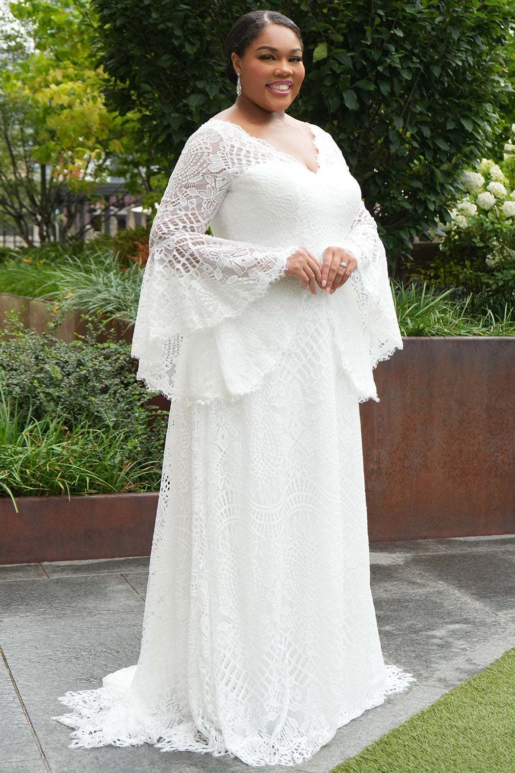 Boho crochet lace plus size wedding dress with V-neckline, illusion lace straps, illusion long flowy bell sleeves, natural wiasltine and slim A-line skirt finished with scalloped eyelash hem.  Available in ivory. Celebrations by Sydney's Closet style CE2604
