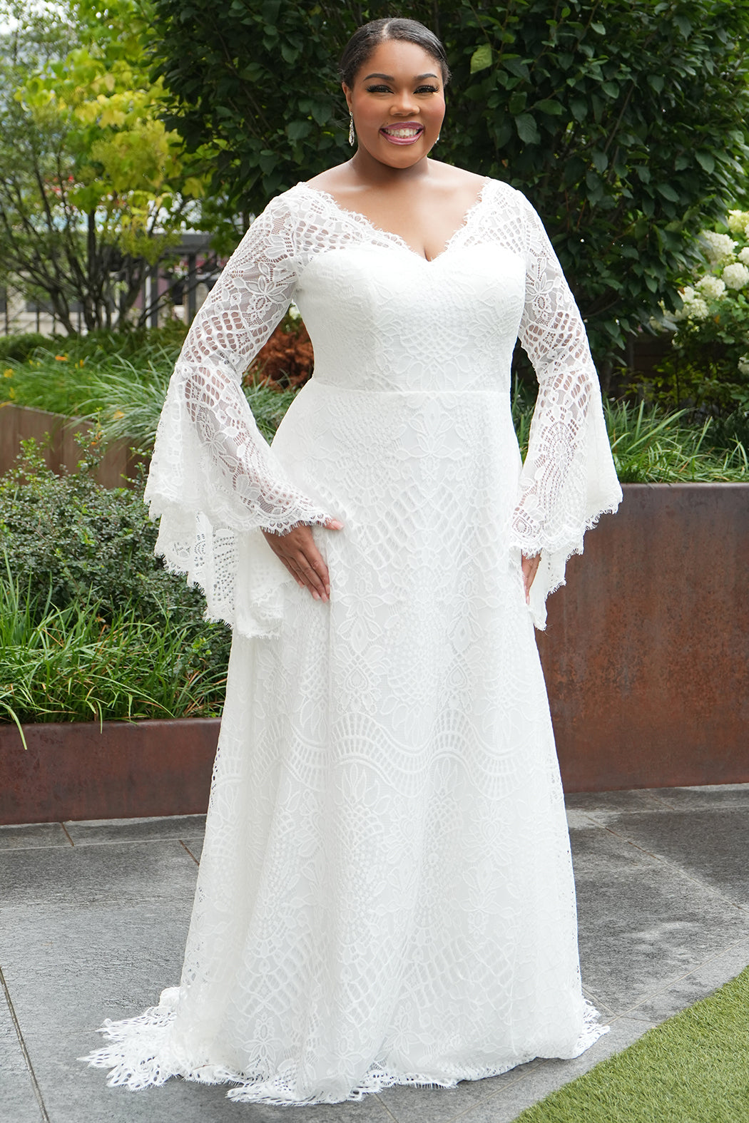 Boho crochet lace plus size wedding dress with V-neckline, illusion lace straps, illusion long flowy bell sleeves, natural wiasltine and slim A-line skirt finished with scalloped eyelash hem.  Available in ivory. Celebrations by Sydney's Closet style CE2604