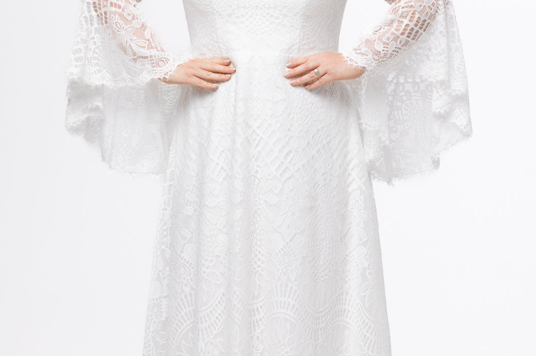 Boho crochet lace plus size wedding dress with V-neckline, illusion lace straps, illusion long flowy bell sleeves, natural wiasltine and slim A-line skirt finished with scalloped eyelash hem.  Available in ivory. Celebrations by Sydney's Closet style CE2604