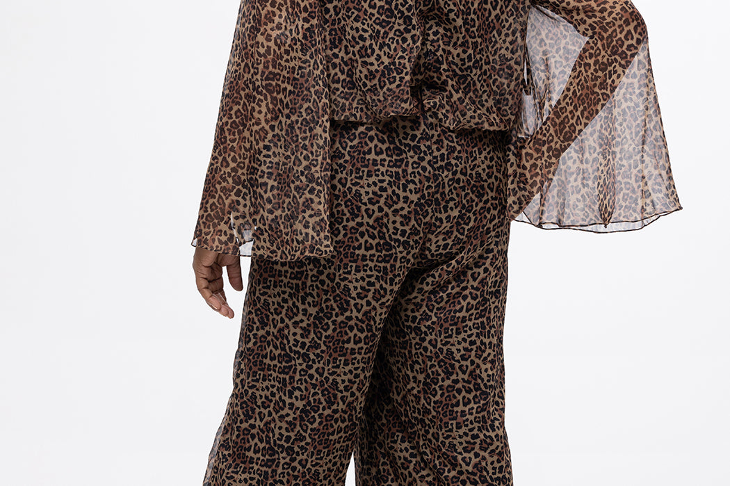 Plus size one-piece animal print jumpsuit. Long flowy chiffon sleeves and blouson bodice, elastic waist, and wide-leg pants. Center back zipper and scoop neckline. CE2607 available in sizes 14-28 in animal print. Celebration's by Sydney's Closet. 