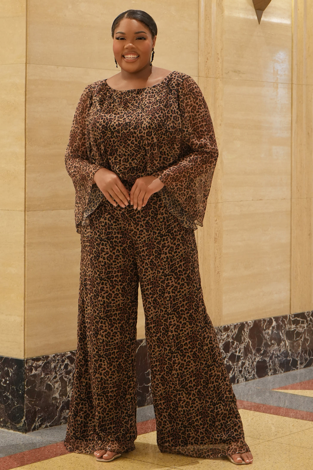 Plus size one-piece animal print jumpsuit. Long flowy chiffon sleeves and blouson bodice, elastic waist, and wide-leg pants. Center back zipper and scoop neckline. CE2607 available in sizes 14-28 in animal print. Celebration's by Sydney's Closet. 