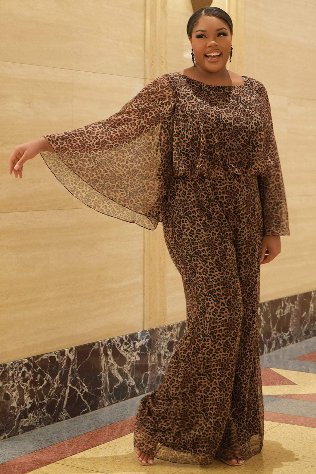 Plus size one-piece animal print jumpsuit. Long flowy chiffon sleeves and blouson bodice, elastic waist, and wide-leg pants. Center back zipper and scoop neckline. CE2607 available in sizes 14-28 in animal print. Celebration's by Sydney's Closet. 