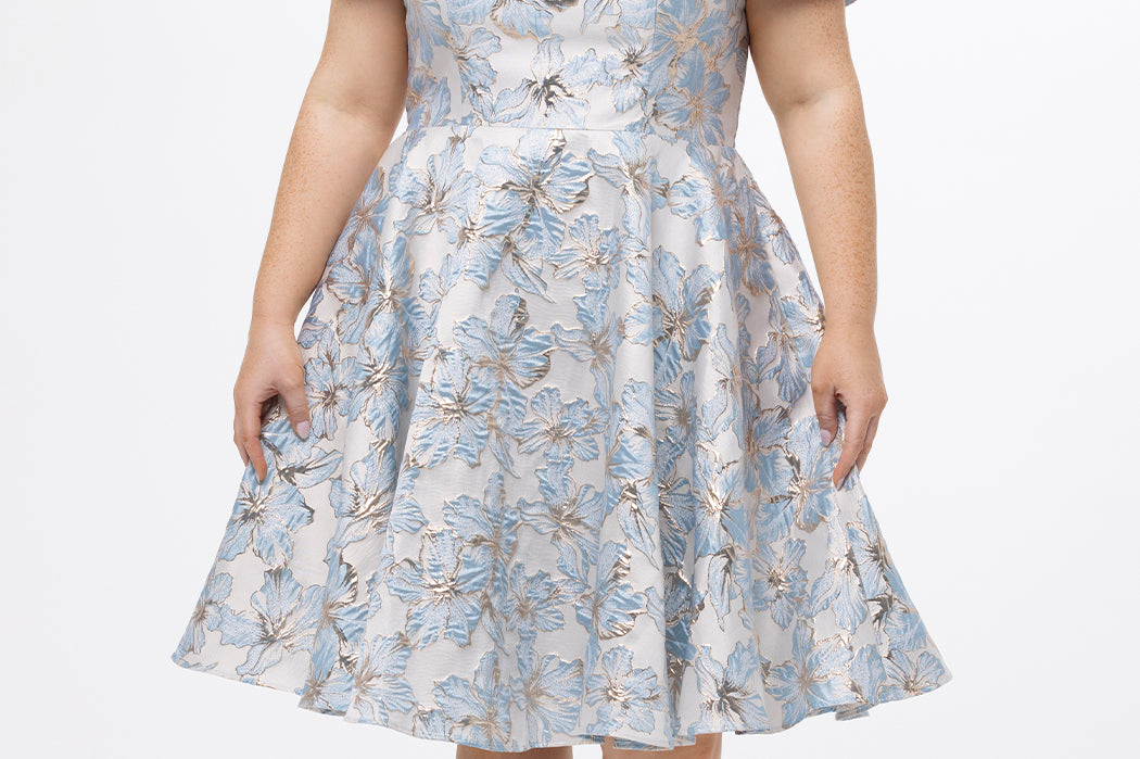 Celebrations by Sydney's Closet CE2610 in Light Blue Floral. 

Plus size knee-length party dress in metallic light blue floral brocde print. Off-the-shoulder neckline, natural waistline and A-line skirt with pockets. 