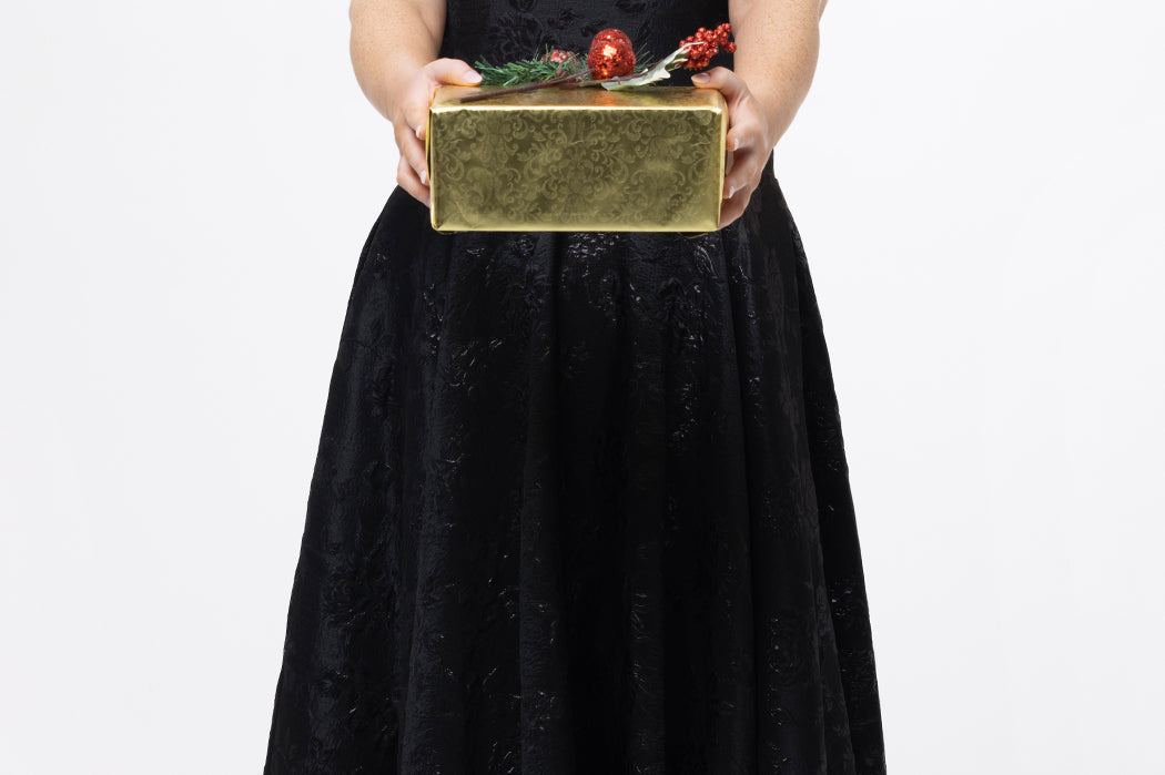 Celebrations by Sydney's Closet Style CE2614 in Black

Plus size maxi length formal dress. One-shoulder neckline with detachable bow at high point of shoulder, natural waistline and A-line skirt with pockets. 

Black floral brocade fabric. 

Shown with model holding a Christmas gift.