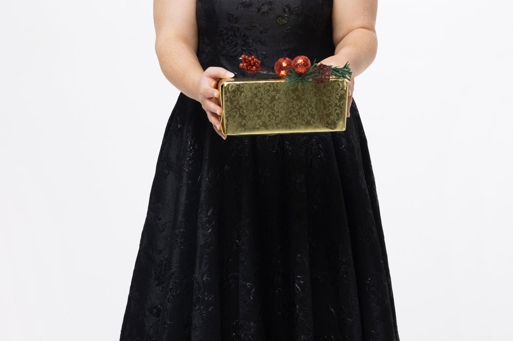 Celebrations by Sydney's Closet Style CE2614 in Black

Plus size maxi length formal dress. One-shoulder neckline with detachable bow at high point of shoulder, natural waistline and A-line skirt with pockets. 

Black floral brocade fabric. 

Shown with model holding a Christmas gift.