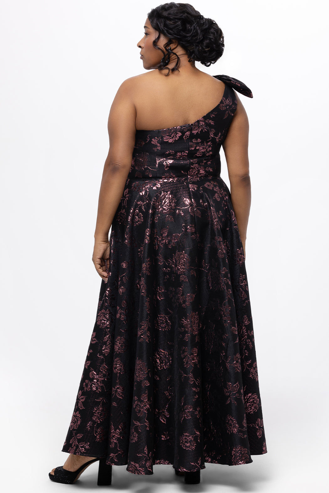 Celebrations by Sydney's Closet Style CE2614 in Pink Rose and Black floral brocade fabric.

Plus size maxi length formal dress. One-shoulder neckline with detachable bow at high point of shoulder, natural waistline and A-line skirt with pockets. 