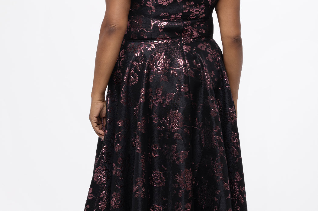 Celebrations by Sydney's Closet Style CE2614 in Pink Rose and Black floral brocade fabric.

Plus size maxi length formal dress. One-shoulder neckline with detachable bow at high point of shoulder, natural waistline and A-line skirt with pockets. 