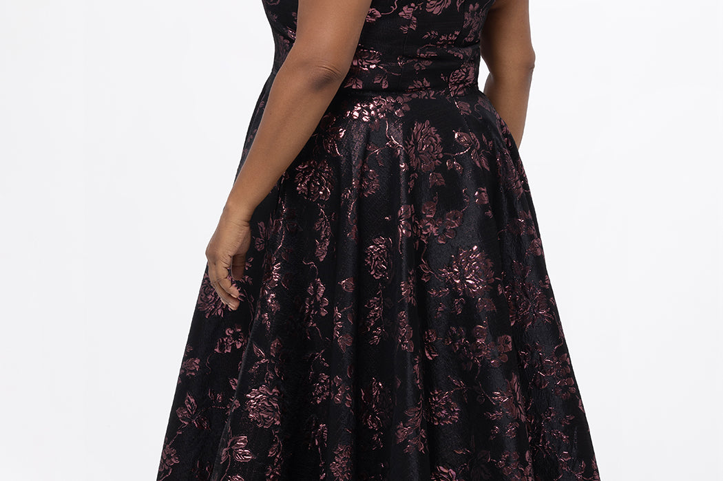 Celebrations by Sydney's Closet Style CE2614 in Pink Rose and Black floral brocade fabric.

Plus size maxi length formal dress. One-shoulder neckline with detachable bow at high point of shoulder, natural waistline and A-line skirt with pockets. 