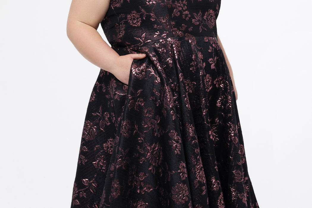 Celebrations by Sydney's Closet Style CE2614 in Pink Rose and Black floral brocade fabric.

Plus size maxi length formal dress. One-shoulder neckline with detachable bow at high point of shoulder, natural waistline and A-line skirt with pockets. 