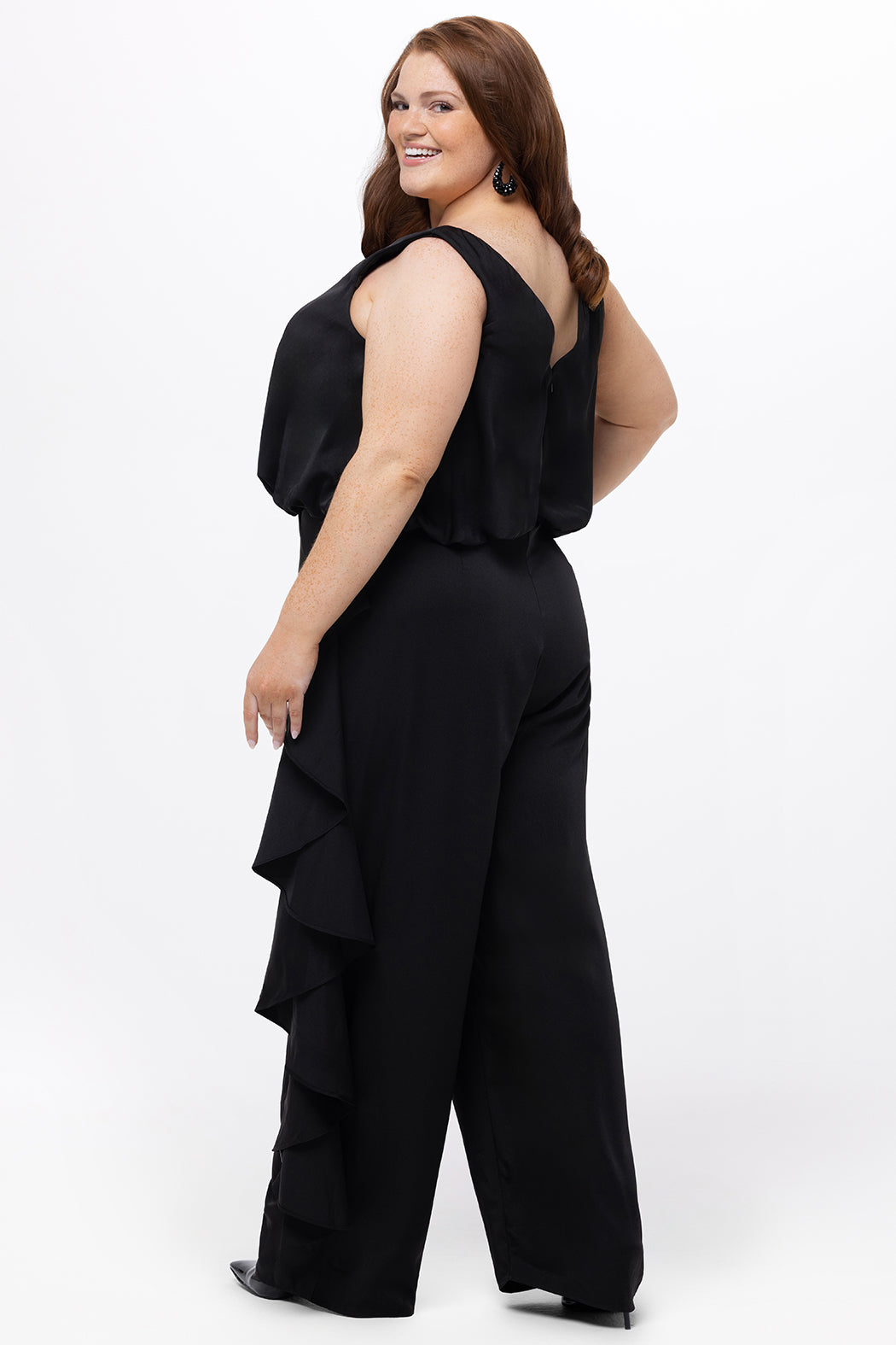 Celebrations by Sydney's Closet Style CE2615 in Black.

One-piece crepe satin jumpsuit with ruffled on outer pants seams. Bra-friendly straps, blouson bodice and wide leg pants. Center back zipper and scoop neckline. 