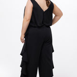 Celebrations by Sydney's Closet Style CE2615 in Black.

One-piece crepe satin jumpsuit with ruffled on outer pants seams. Bra-friendly straps, blouson bodice and wide leg pants. Center back zipper and scoop neckline. 