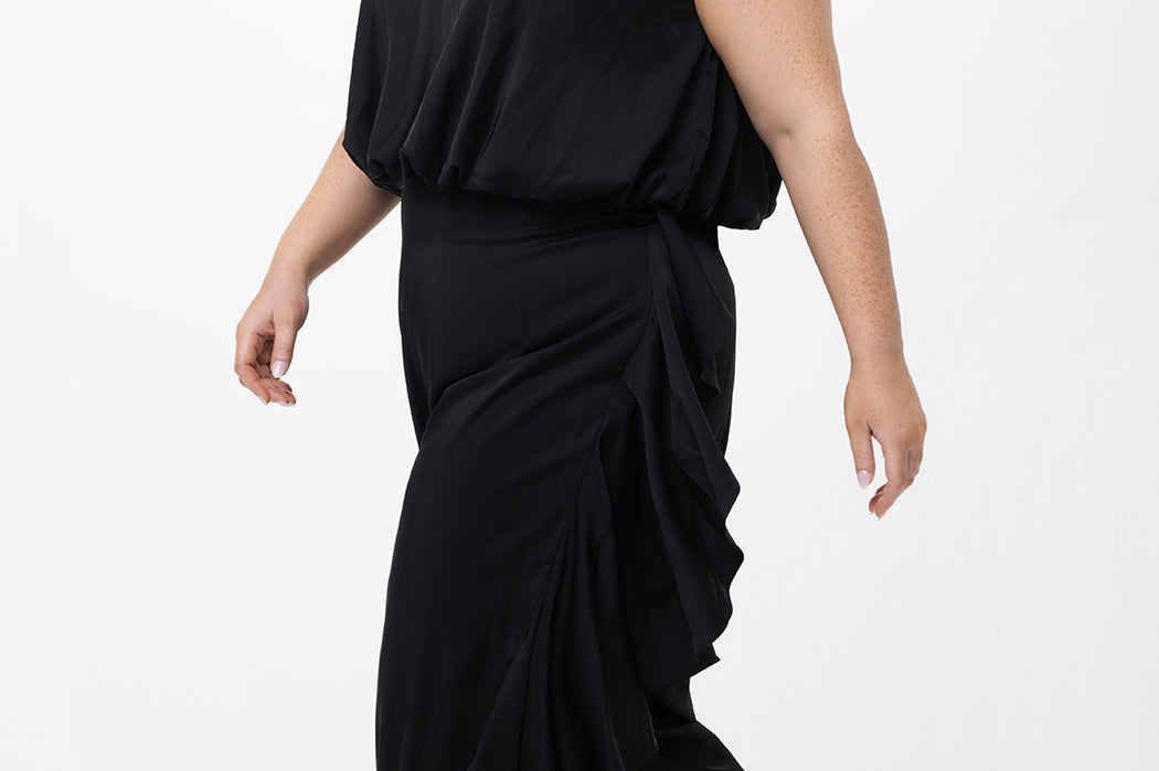 Celebrations by Sydney's Closet Style CE2615 in Black.

One-piece crepe satin jumpsuit with ruffled on outer pants seams. Bra-friendly straps, blouson bodice and wide leg pants. Center back zipper and scoop neckline. 