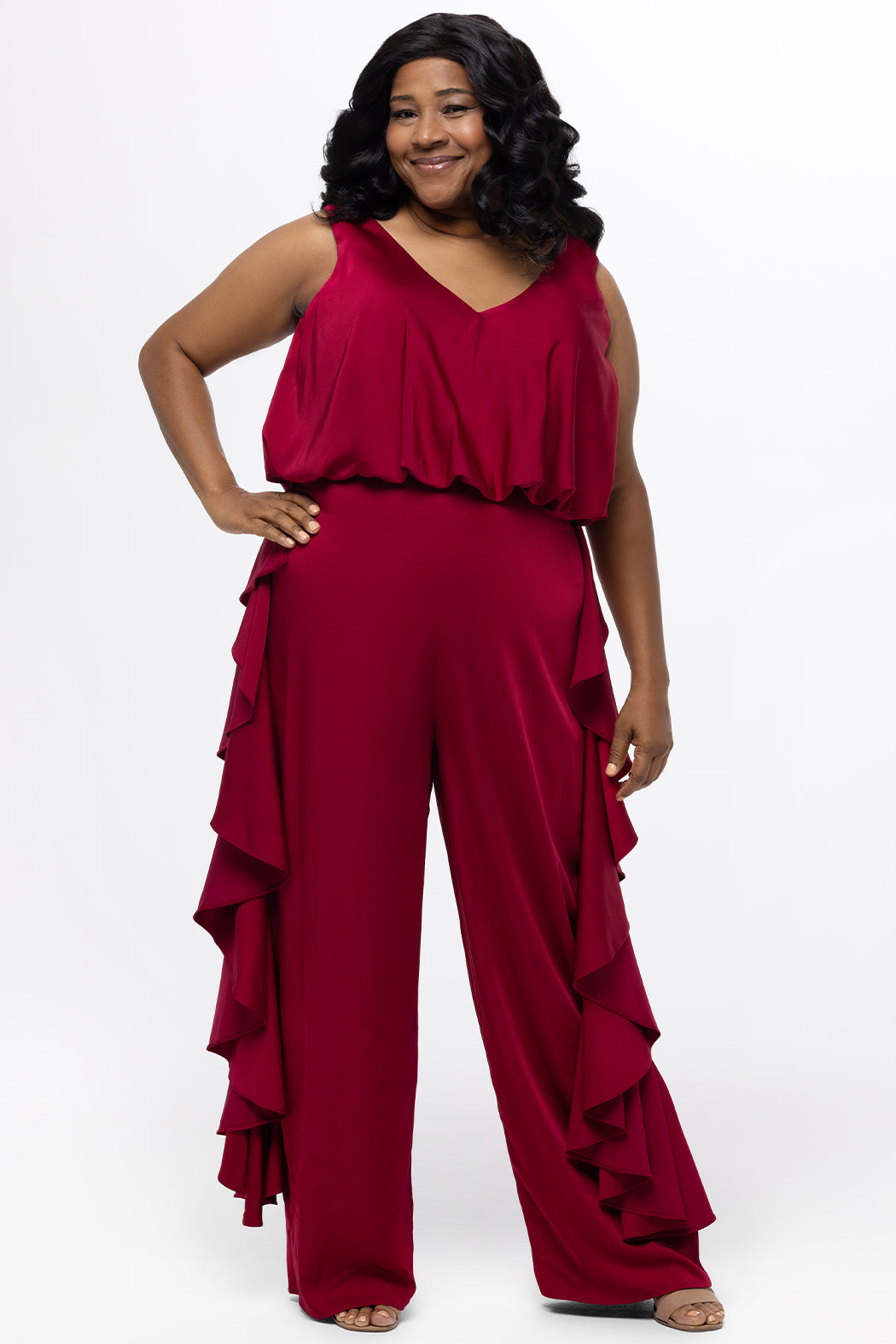 Celebrations by Sydney's Closet Style CE2615 in cherry red.

One-piece crepe satin jumpsuit with ruffled on outer pants seams. Bra-friendly straps, blouson bodice and wide leg pants. Center back zipper and scoop neckline. 