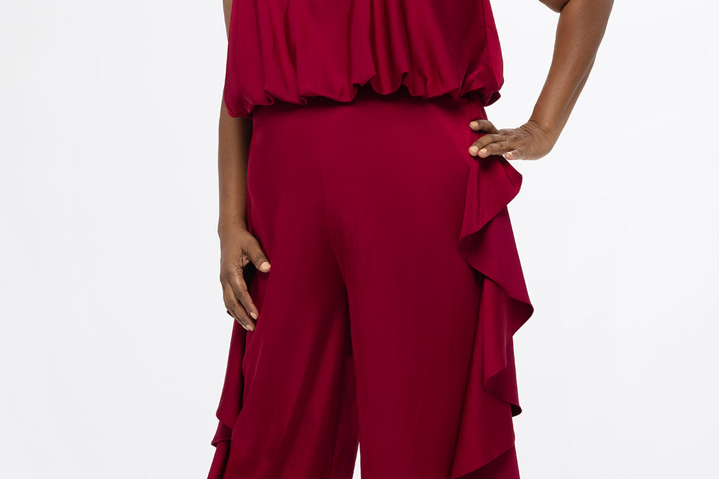 Celebrations by Sydney's Closet Style CE2615 in cherry red.

One-piece crepe satin jumpsuit with ruffled on outer pants seams. Bra-friendly straps, blouson bodice and wide leg pants. Center back zipper and scoop neckline. 