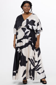 Celebrations by Sydney's Closet Style CE2620 in black/white geometric print. 

Plus-size model wearing a flowing black-and-ivory abstract print maxi dress with a V-neckline, draped bodice, elbow-length sleeves, and a softly flared skirt, photographed against a white background.