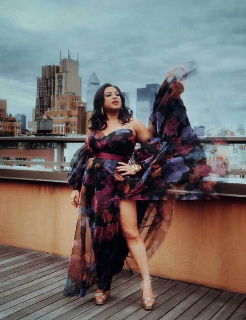 Woman in a colorful dress standing on a rooftop with city skyline in the background