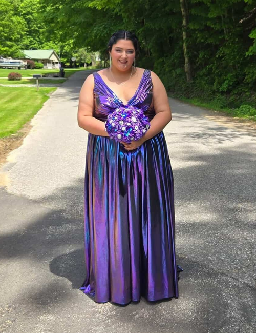 Woman in a purple dress holding a bouquet on a road with greenery in the background