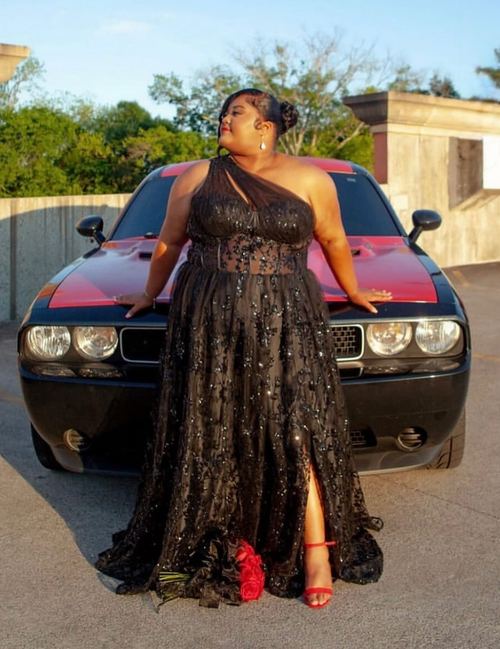 Woman in a black dress standing in front of a red and black vehicle.
