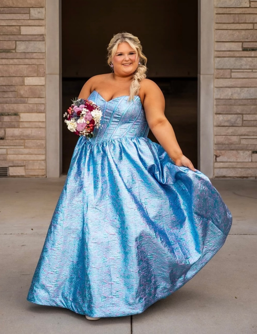 Woman in a blue formal gown standing in front of a brick wall.