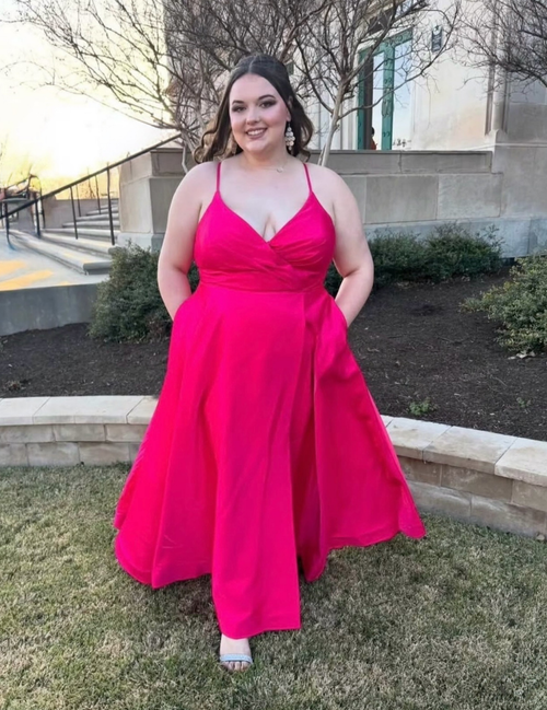 Woman in a bright pink dress standing outdoors with a building and trees in the background.