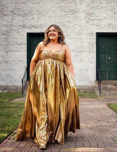 Woman wearing a gold dress standing in front of a brick building.