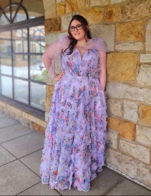 Woman in a purple floral dress standing against a stone wall.