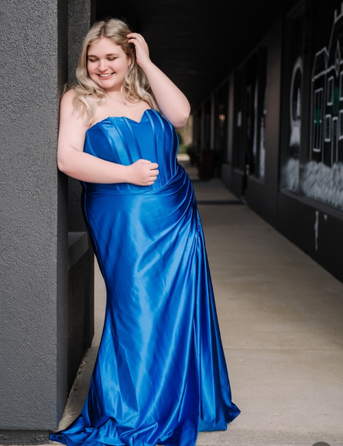 Woman in a blue strapless gown standing against a wall.