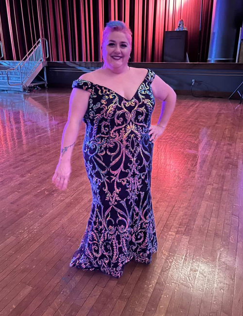 Woman in a patterned dress standing on a wooden floor with red curtains in the background